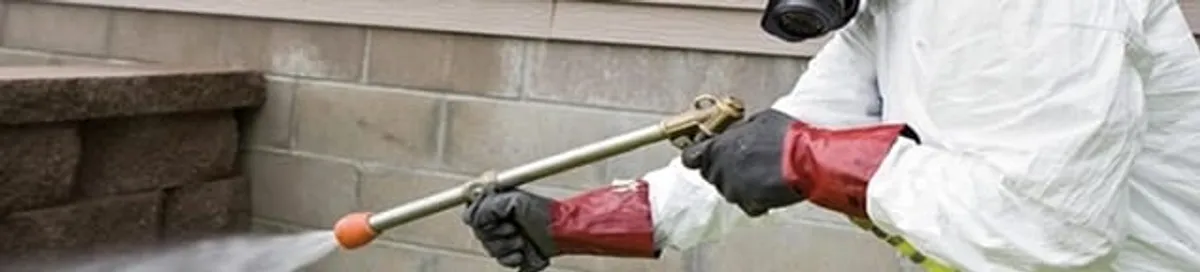 Pest control technician applying exterior insect treatment along a home foundation in Ogden, UT