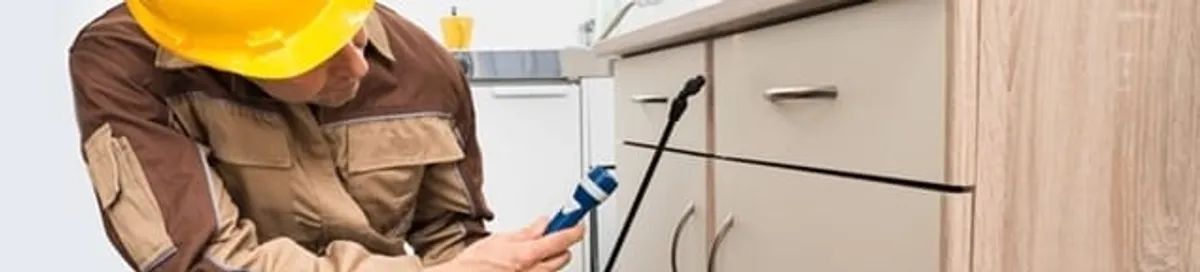 Roach exterminator applying treatment under kitchen cabinets in Ogden, UT