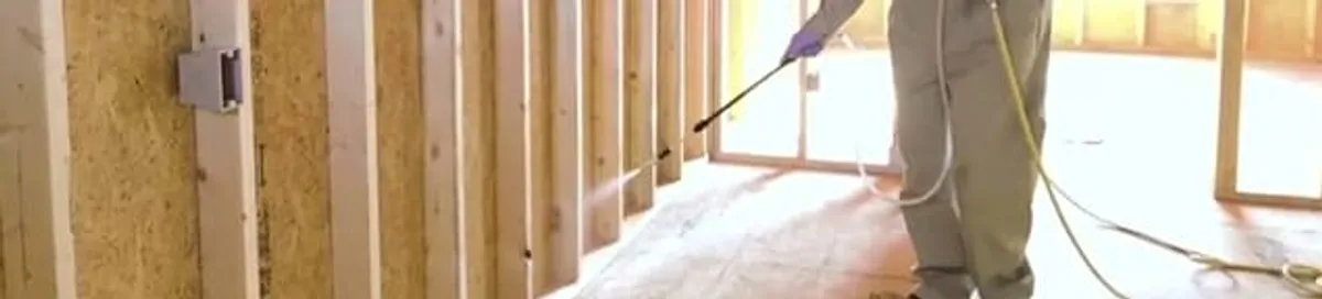 Termite treatment technician applying spray along framing and unfinished walls in Ogden, UT